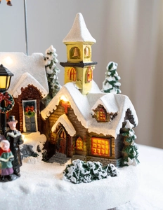 Close-up of lighted Christmas village house with snow, miniature trees and figures
