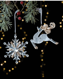 Detail of transparent acrylic snowflake and reindeer ornaments with gold sequins on pine branch