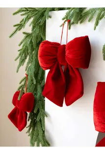 Close-up of a premium red velvet Christmas bow hanging with green pine needle accents