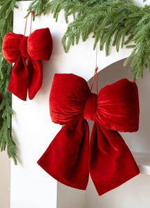 Detail of red velvet Christmas bows hanging from green pine branches for festive decor