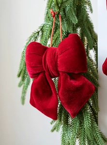 Detailed close-up of a red velvet Christmas bow hanging on a green festive tree branch