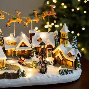 Lighted Christmas village house with snow details and animated reindeer on a table