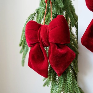 Red velvet Christmas bow ornament hanging on a pine tree branch for holiday decor