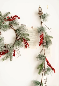 Detail of Christmas wreath and pine needle garland with red berries and snowy pinecones