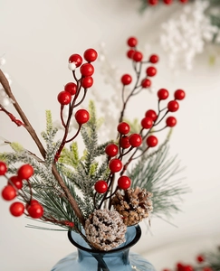 Close-up of red berries and frosted pine cones in a blue glass vase for Christmas decor