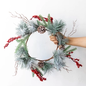 Christmas wreath with artificial pine needles, red berries and pinecones on white wall