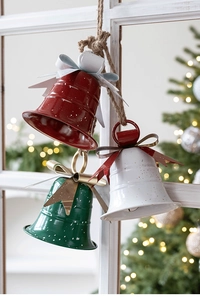 Close-up of metal Christmas bells with rustic snow finish hanging on a white window