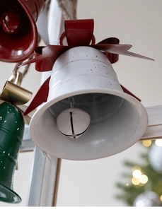 Close-up of a white metal Christmas bell with golden speckles and red satin bow detail
