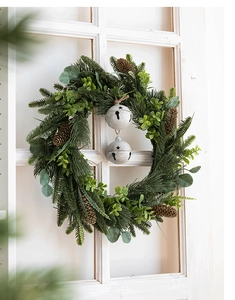 Detail of Christmas wreath with green pine needles and vintage white metal bells on a white window