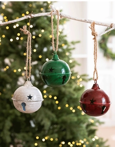 Three vintage metal Christmas bells with star cutouts hanging on a rustic branch