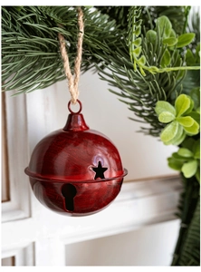 Detail of red metal Christmas bell with star cutouts hanging on a pine branch
