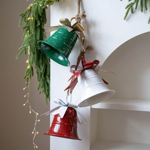 Three metal Christmas bells in red white and green with jute rope on pine tree