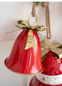 Close-up of red metal Christmas bell with gold bow and snowflake detail on jute rope
