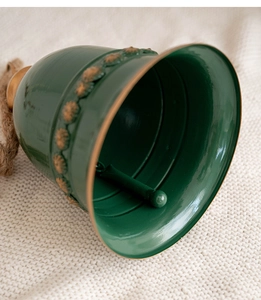 Close-up of green vintage iron Christmas bell with gold floral relief and hemp rope