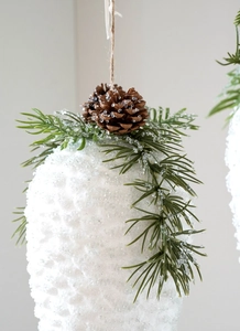 Macro view of snowy pinecone ornament with green needles and rustic hanging rope