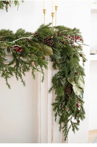 Detail of green Christmas garland with pine cones and red berries on a white fireplace