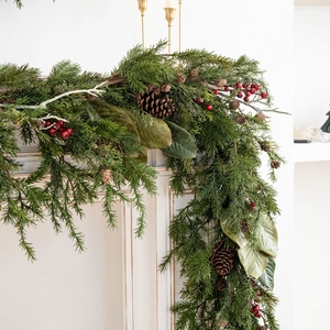 Lush Christmas garland with pine cones and red berries draped over a white fireplace mantel