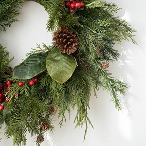 Premium Christmas wreath with pine branches, red berries and pinecones on a white wall