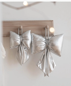 Silver satin Christmas bows hanging on a minimalist wooden rack with soft bokeh lights