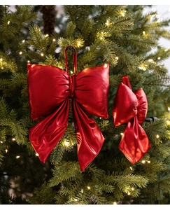 Close-up of vibrant red metallic velvet Christmas bow hanging on a lit Xmas tree