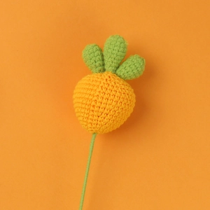 Detail of a handmade crochet carrot charm with orange yarn and green leaf accents