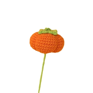 Handmade crochet orange pumpkin decoration with green leaves on white background