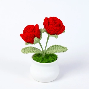 Detailed close-up of handmade crochet red roses in a white pot with knit leaf textures