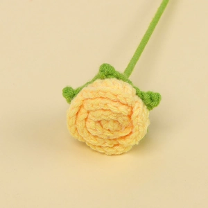 Close-up of a handmade yellow crochet rose with green leaves and a knitted stem detail