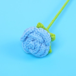 Close-up of handmade crochet blue rose flower with detailed yarn texture and green leaves