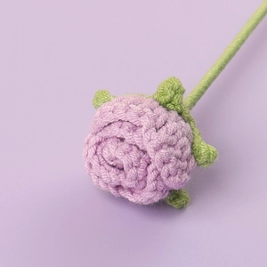 Macro detail of a handmade crochet purple rose with textured petals and green stem