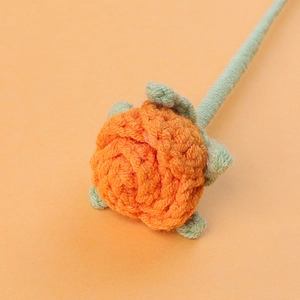 Macro shot of handmade crochet orange rose with green stem and leaves on warm background
