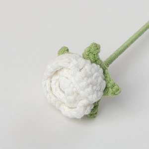 Close-up of handmade white crochet rose with green stem showing knitted texture details