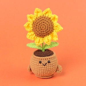 Handmade crochet sunflower potted plant with cute smiling face on a bright orange background