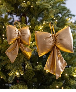 Close-up of golden plush fabric Christmas bows hanging on a green tree with warm lights