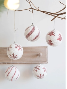 Close-up of white frosted Christmas ornaments with red glitter snowflake and tree patterns
