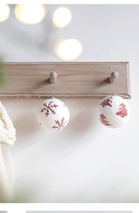Close-up of white flocked Christmas ball with red snowflake pattern on wooden stand
