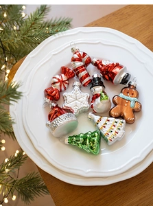 Close-up of festive glass ornaments including Santa and snowman on a white ceramic plate