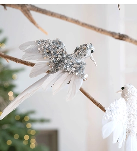 Dettaglio di ornamenti a colibrì con paillettes e piume bianche su un ramo di Natale