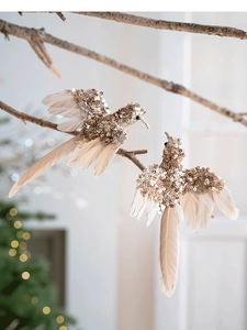 Dettaglio di colibrì con paillettes oro champagne e piume bianche su un ramo decorativo