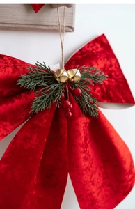 Detail of red velvet Christmas bow with green pine needles, gold bells and red berries