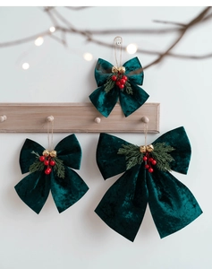Three dark green velvet Christmas bows with gold bells and red berries on a wooden hook