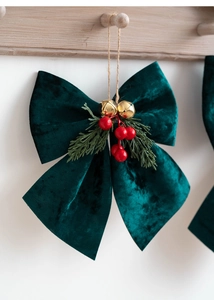 Macro view of dark green velvet Christmas bow with gold bells and red berries