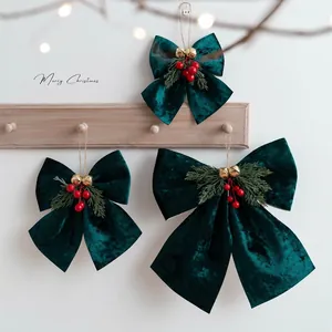 Three dark green velvet Christmas bows with pine needles and bells on a wooden hanger