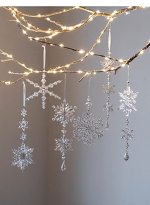 Detail of acrylic snowflake ornaments with beads hanging on branches with warm lights