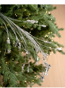 Silberner Paillettenzweig auf einem Weihnachtsbaum mit warmen Bokeh-Lichtern