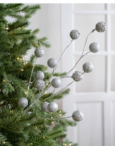 Close-up of sparkling silver sequined berry stems on a lit Christmas tree branch
