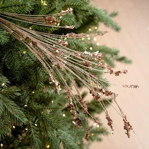 Roségoldene Weihnachtsglitzerzweige mit Pailletten auf einem beleuchteten Tannenbaum