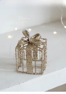 Gros plan d'un ornement de boîte cadeau pailleté doré avec cadre en métal et ruban blanc