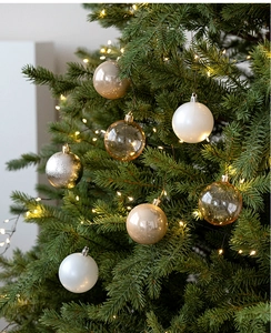 Detail of champagne gold and white Christmas ornaments hanging on a festive tree with warm lights