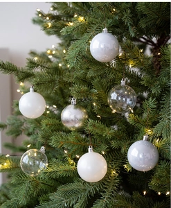 Close-up of assorted white and silver Christmas balls hanging on a lighted tree